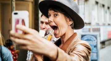 A tourist taking a selfie while eating an ice cream and grinning excitedly.