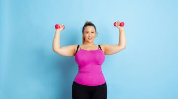 Young caucasian plus size female model's training on blue background. Concept of sport, human emotions, expression, healthy lifestyle, body positive, equality. Training with the weights, copyspace.