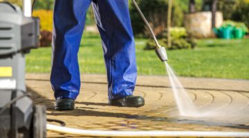Worker and Pressure Washer. Men Wearing Rain Coat Cleaning Brick Paths Using Powerful Water Sprayer.