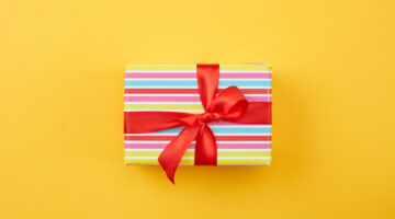 wrapped gift box with red ribbon bow on yellow paper background, top view