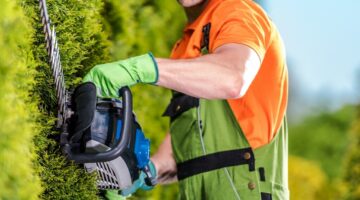 Hedge Trimmer Garden Work. Caucasian Gardener with Trimming Power Tool Closeup Photo.