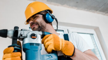 selective focus of handyman in helmet and yellow gloves using hammer drill