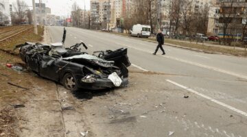 A man crosses the road near the civil vehicle driven-through by Infantry Fighting Vehicle russian saboteur group before being eliminated in Kyiv, Ukraine, February 25, 2022. (Photo by Sergii Kharchenko/NurPhoto via Getty Images)