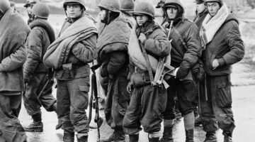THE FALKLANDS CONFLICT, APRIL - JUNE 1982 (FKD 303) Argentine prisoners wait to hand in their weapons and other equipment at Port Stanley after the surrender.  Most are carrying blankets. Copyright: © IWM. Original Source: http://www.iwm.org.uk/collections/item/object/205189225