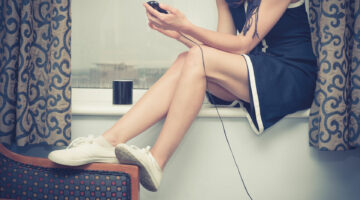 39966304 - a young woman is sitting on a window sill and is charging her smartphone