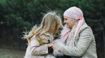 A woman with cancer is  next to her daughter. A girl is hugging a woman happy