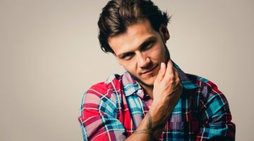 Fashion portrait of a handsome man with trendy hairstyle in a stylish shirt on light green background