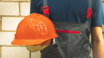 Man in overalls holds safety helmet outdoor