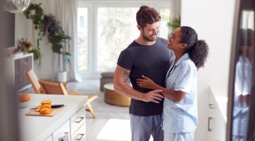 Loving Couple Wearing Pyjamas Hugging In Kitchen At Home Together