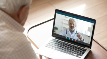 Back view of mature man have video call consultation with male doctor using laptop Webcam, close up of elderly male patient talk speak with GP or physician at home, discuss illness, consult online
